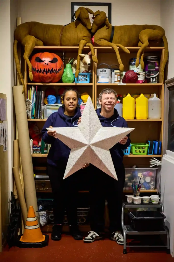 Two EGO artists holding up a giant star in front of a shelf full of art equipment.