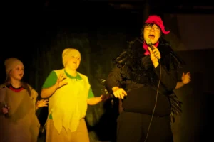 An actor dressed as a turkey singing into a microphone, while two other actors sing along behind him