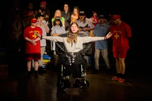 Actor in wheelchair with arms out infront of ensemble