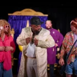 Two actors dressed as women. The middle actor is dressed as prince