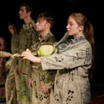 Actors lined up. first actor blowing into pipe