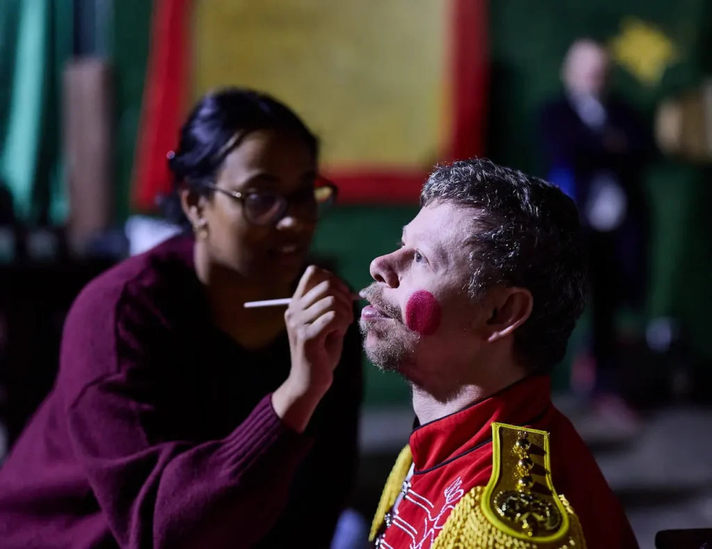 A volunteer paints rosy cheeks onto an EGO actor's face.
