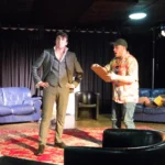 Two actors on stage. One actor has a clipboard