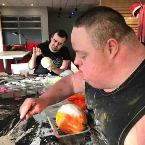 Two EGO artists focusing on painting two orange paper mache balls.