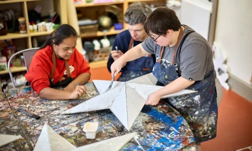 Three EGO artists at a paint-covered table paint a large cardboard five-point star.