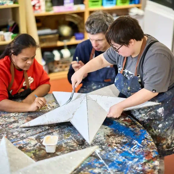 Three EGO artists at a paint-covered table paint a large cardboard five-point star.