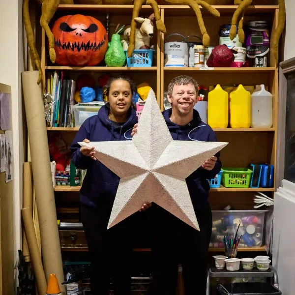 Two EGO artists holding up a giant star in front of a shelf full of art equipment.