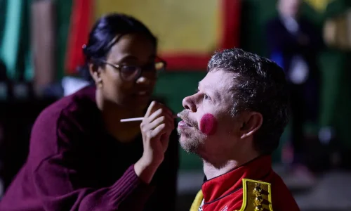A volunteer paints rosy cheeks onto an EGO actor's face.