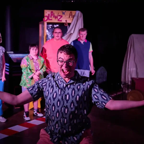 An actor cheers in victory while other actors watch from behind.