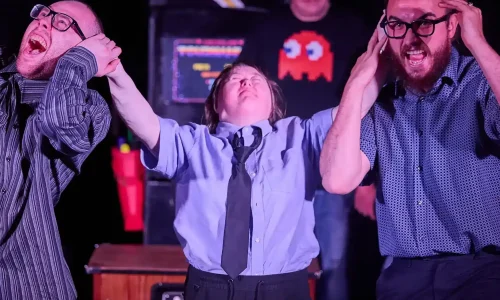 An actor with Down's syndrome dressed as police holds the ears of two other actors who are pretending to scream in pain.