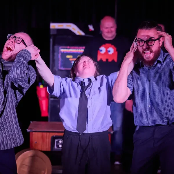 An actor with Down's syndrome dressed as police holds the ears of two other actors who are pretending to scream in pain.