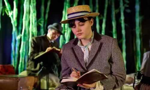 An actor in Victorian costume writes in a notebook.