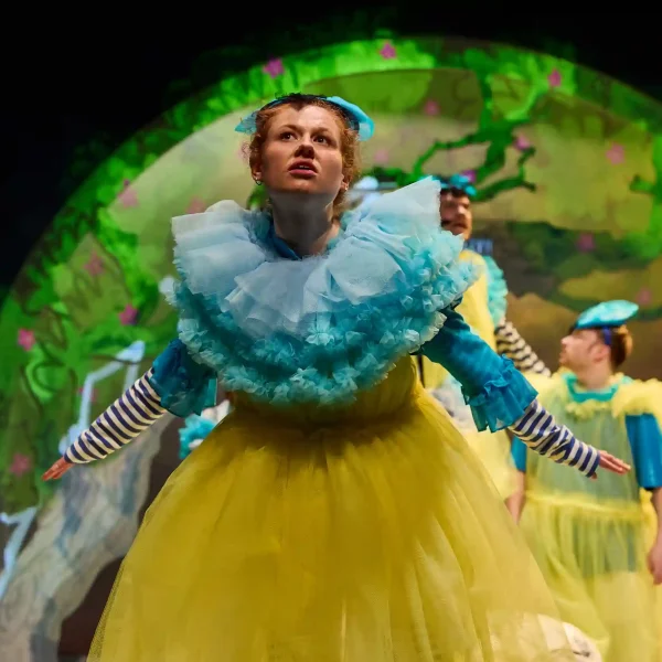 An actor dressed as a blue tit with a yellow dress and a giant light-blue ruff.