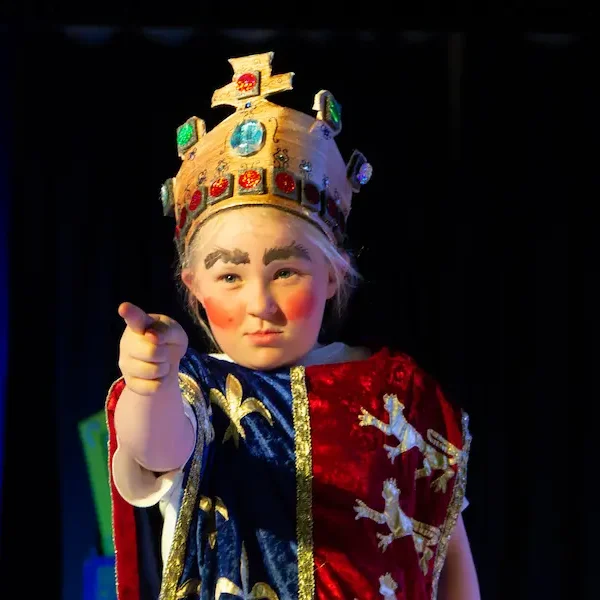 A young actor dressed as a king and pointing.