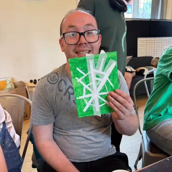 An EGO artist holds up a spider web design he has made using white tape and green felt tip pen.