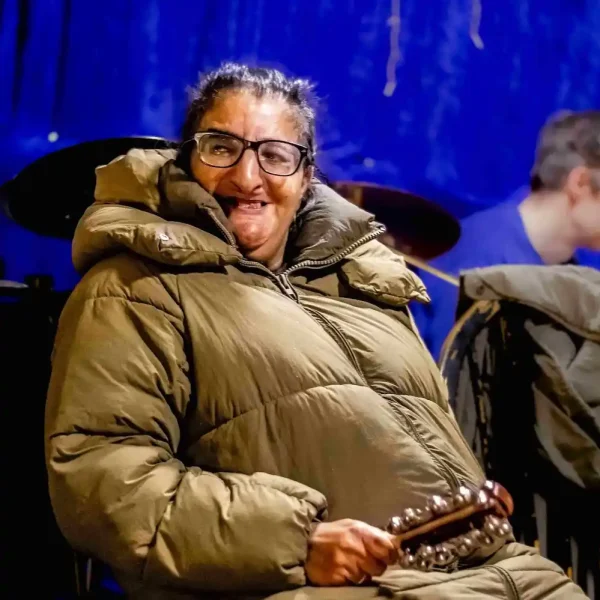 A woman wearing a big quilted coat and smiling at the camera, holding a stick with bells on.