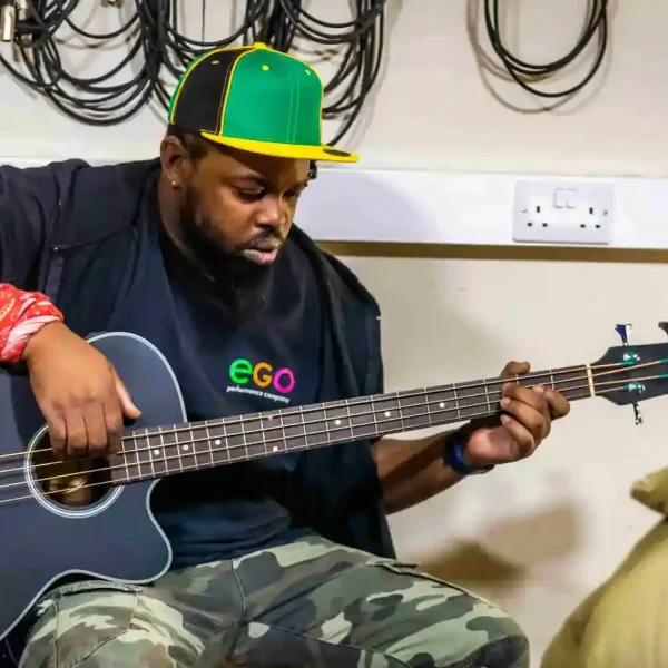 A man wearing a cap and playing a guitar in a music studio.