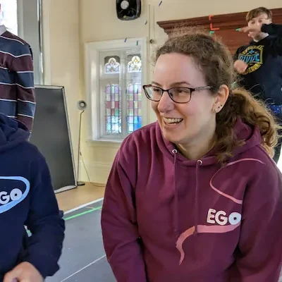 Two actors wearing EGO hoodies smiling during a rehearsal inside EGO's theatre studio.