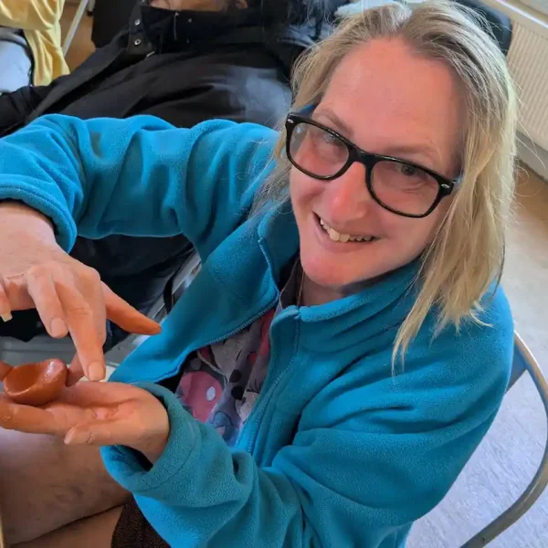 An EGO artist smiles while holding a small ball of brown clay that she is moulding.