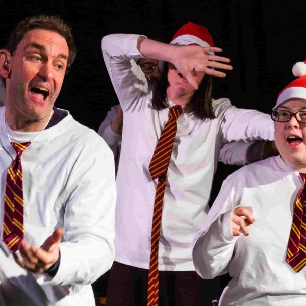 Four actors wearing white shirts, ties and Santa hats and dancing.