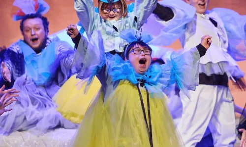 Four actors with learning disabilities or neurodivergence dressed as birds and cheering with their arms up.