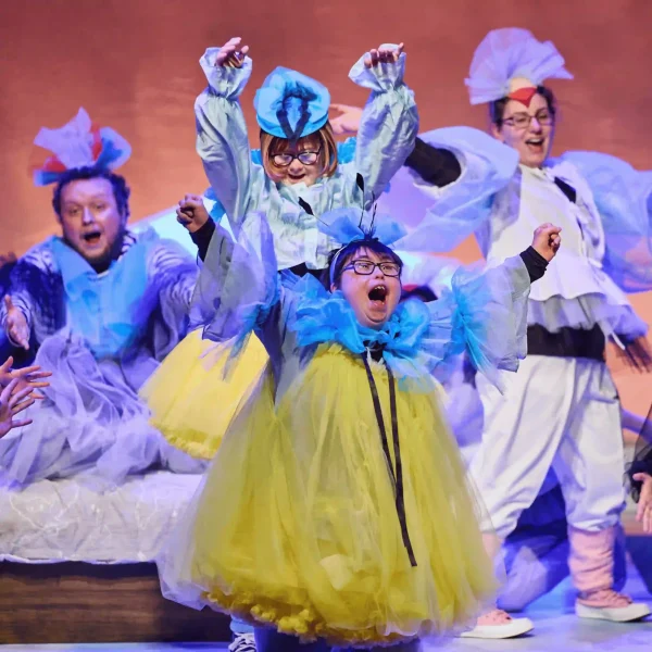Four actors with learning disabilities or neurodivergence dressed as birds and cheering with their arms up.