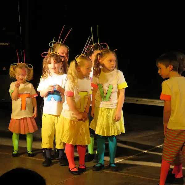 Young children performing on stage in neon coloured costumes.
