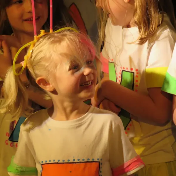 A young girl smiling surrounded by other young actors on stage