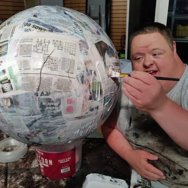 An EGO artist proudly using a paint brush to cover a giant paper mache sphere with PVA glue.