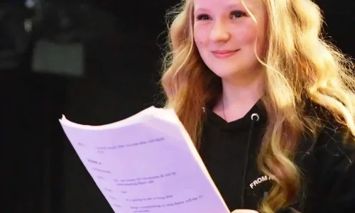 A teenage girl holding a script and smiling in a theatre studio.
